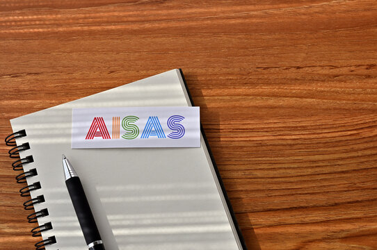 There is a card on the table with "AISAS" (Attention, Interest, Search, Action, Share) written on it, on a notebook.