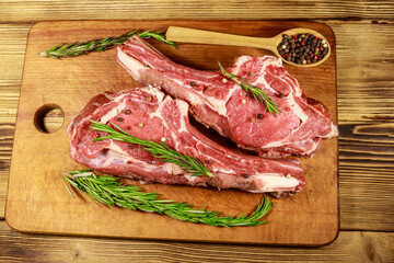Raw fresh beef rib eye steaks on bone with spices and rosemary on wooden table. Top view