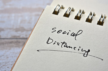 At the edge of the notebook, "Social Distancing" is written. Close-up.