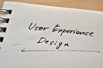 At the edge of the notebook, "User Experience Design" is written. Close-up in direct sunlight.