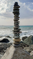 Tower of balancing stones on the background of the sea, waves and beach. Vertical image