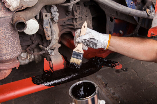 A car mechanic cleans and maintains the engine chassis of an old car against corrosion and protects it with a preparation