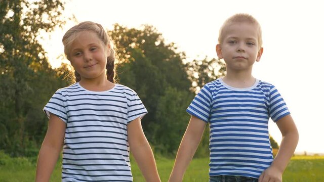 Happy children walk in a green park on a summer day. Kids in the park holding hands. The concept of a child's dream of happiness. Boy and girl kids walk in the fresh air.