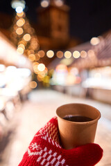 Christmas Market in European small city. Hand holding a cup of mulled wine with blurred background of winter wonderland, a