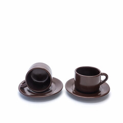 Two small porcelain brown coffee cups. One is on a saucer, the other is lying. Isolated over white background. Side view.