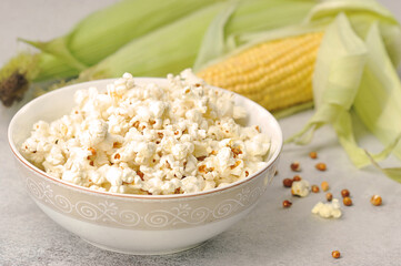 ears of corn and prepared popcorn in a bowl on a grey background