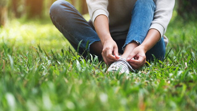 Closeup image of a woman sitting and tying shoelaces in the park