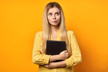 Surprised young woman in a hat holds a book on a yellow background.