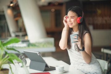 Portrait of female with headphone relaxing with coffee cup while working with mock up tablet in cafe.