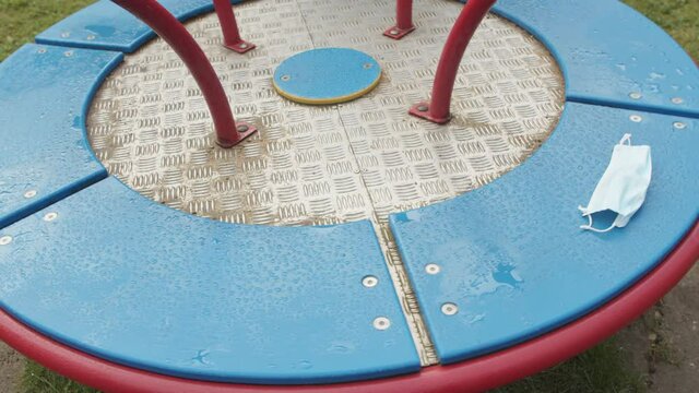 Face mask left on rotating roundabout. A deserted playground on a rainy day, medium shot