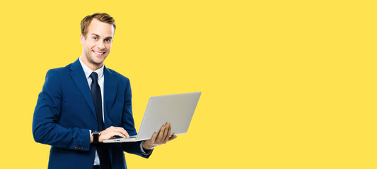 Portrait image - smiling businessman in blue confident suit, working with laptop, isolated against yellow background. Handsome man at studio concept picture. Copy space for text.