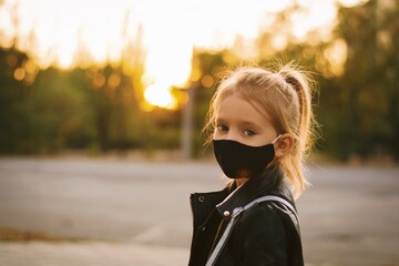 Child, girl of European appearance wearing a barrier black mask outdoors. Pandemic concept.