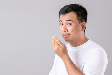 Man checking his breath with hand. Portrait asian man are sleepy in studio shot on grey background