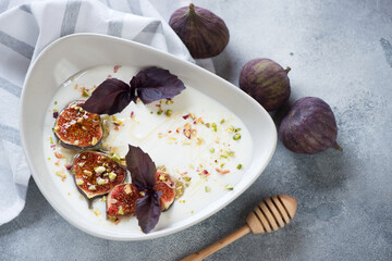 Greek yogurt served with sliced fig fruits, honey and chopped nuts in a grey bowl, horizontal shot on a light-blue stone background