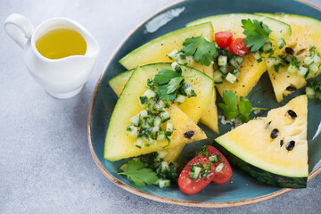 Slices of yellow watermelon topped with herbed chopped cucumber and served on a turquoise plate, close-up