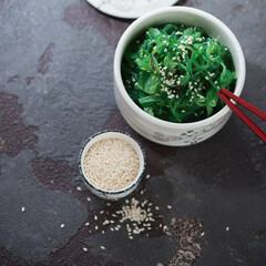 White bowl with seaweed salad and sesame, high angle view on a brown stone background, studio shot