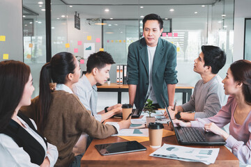 Focus on asian man(boss or manager)standing in group brainstorm meeting in office.Businesspeople discussing with paperwork for business plan,Corporate of modern colleague