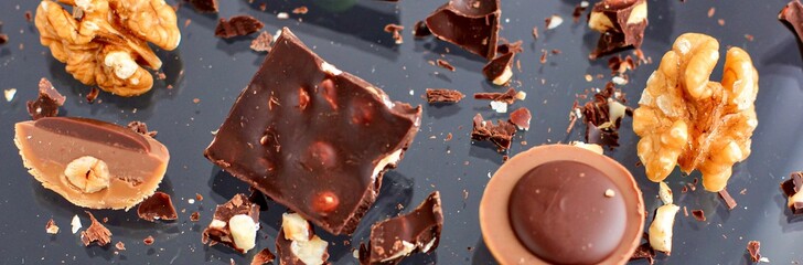 Sweets, pieces of chocolate and nuts on a dark background. Banner.