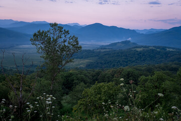 Fototapeta na wymiar Early morning one hour before dawn. Silhouettes of mountains in the morning haze, grass and trees in the foreground. Lagonaki Plateau, Republic of Adygea, Russia