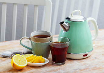 Tea party for couple. Retro style turquoise electric kettle, two cups of tea and sliced lemon on wooden kitchen table..