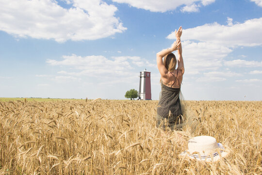 Happy woman with rised hands stand in barley field oposite beacon. Summer wallaper