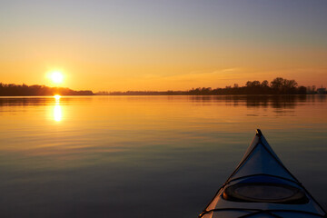 View from bow (prow) of blue kayak at colorful sunset over Danube river at autumn time