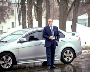 A business man in a strict blue suit by a car on the road in winter. Transport and auto. Business. Copy space on the left