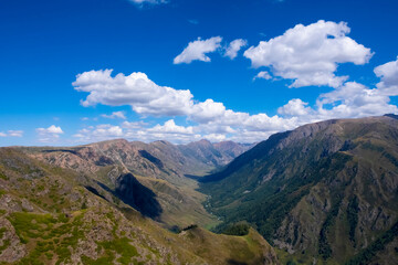 Obraz premium Mountain gorge landscape with cloudy blue sky. Summer nature landscape. River valley panorama. Kora river gorge in Kazakhstan, way to Burkhan bulak waterfall. Tourism in Kazakhstan concept.