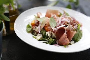Salad with Parma ham, tomatoes, yellow beetroot, and vinaigrette sauce.
Appetizing dish served on a white plate. culinary photography.
