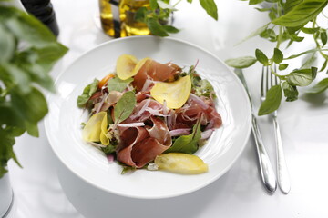 Salad with Parma ham, tomatoes, yellow beetroot, and vinaigrette sauce.
Appetizing dish served on a white plate. culinary photography.
