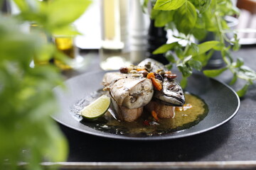 Roasted mackerel. Whole fish served with garlic, olives, and lemon.
Appetizing dish served on a black plate .Culinary photography, food photography.