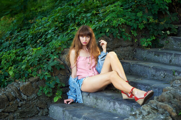 Portrait of a young woman in denim shorts sitting on the steps of an old stone staircase