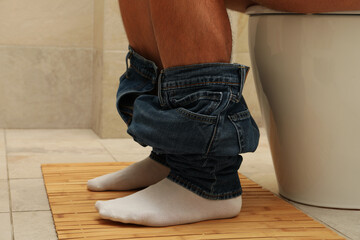 A man sits with his pants down on the toilet