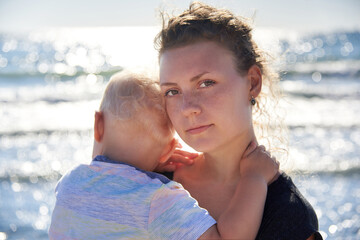 Mom gently hugs her little son on the seashore.