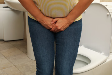 Woman holding groin in bathroom near toilet bowl