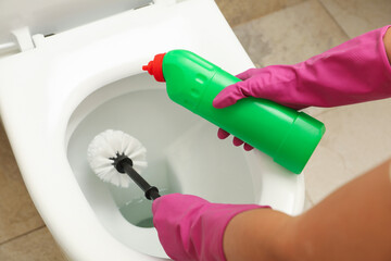Woman in rubber pink gloves cleans toilet bowl with brush