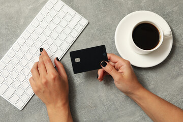 Female hand hold card on gray background with keyboard and coffee