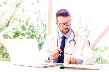 Careworn male doctor working on laptop and desk in the hospital