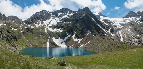 Panoramic view of turquoise blue mountain lake Grunausee in alpine landscape with green meadow and snow-capped mountain peaks. Tyrol, Stubai Alps, Austria, summer sunny day - Powered by Adobe