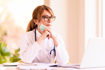 Thinking female doctor working on laptop at desk at the doctor's office