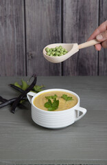 Soup-mashed peas and beans in a white Cup on a gray wooden background, hand with a spoon with peas over a Cup of soup . Place for a copy space
