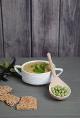 Soup-puree of peas and beans in a white Cup on a gray wooden background with grain crackers, a spoon with peas next to the Cup . Place for a copy space