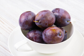 Ripe plums in a white bowl on a wooden white table