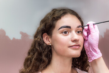 Obraz premium Portrait of young beautiful girl whose eyebrows are plucked. Eyebrow shaping in a beauty salon. Close up of eyebrow and hand of eyebrow artist