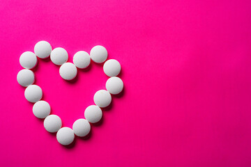 many white pills from heart on a pink background. accept gifts concept. Cardiology or love concept