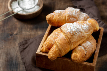 Croissants. Croissants and cappuccino in a wooden box on a brown background. French breakfast