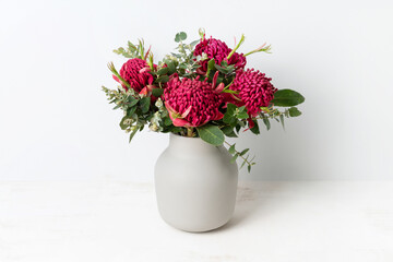 A bunch of Australian native red waratah flowers and eucalyptus leaves, in a stylish ceramic grey...
