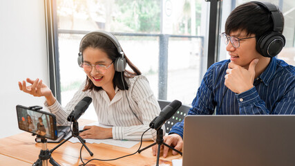 Asian Man and woman podcasters in headphones recording content with colleague talking to microphone...