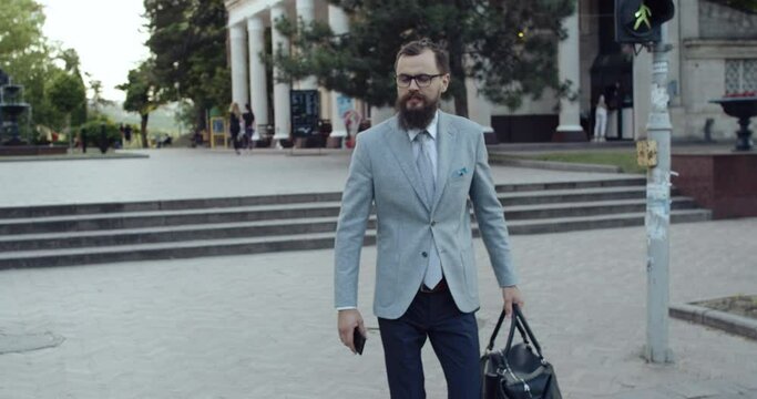 A businessman with a beard and glasses crosses the street on the crosswalk.