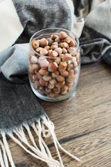 Autumn composition with hazelnuts in a glass jar on a wooden background next to a plaid. Organic hazelnut. Close-up.